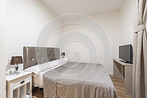 Double bedroom with headboard upholstered in shiny gray fabric, white wooden bedside tables with twin lamps and matching curtains