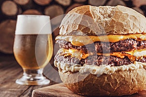Double burger with cheddar cheese, a glass of beer and firewood pile in background - Close-up