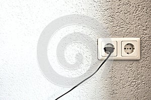 Double electrical power European socket with black cable and plug on white wall space for text