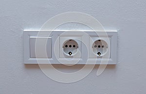 Double electrical wall socket with light switch on white wall