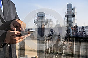 Double exposure of businessman checking oil refinery industry plant by smart phone