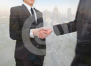Double exposure of businessmen shaking hands with blur city.