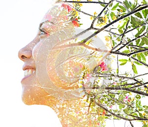 Double exposure close up profile portrait of a young pretty woman interwoven with tree branches and delicate colorful flowers