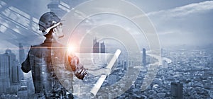 Double exposure, Construction engineer holding blueprint on construction site and blue city background