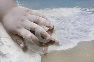 Double exposure effect. Child hand and starfish on natural sea background.