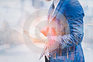 Double exposure image of businessman using digital tablet on city blurred background. Business success concept