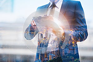 Double exposure image of businessman using digital tablet on city blurred background. Business success concept