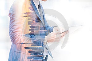 Double exposure image of businessman using digital tablet on city blurred background. Business success concept