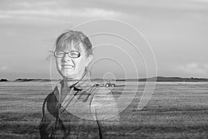 Double exposure image of a woman standing in a field with a tractor on the land.