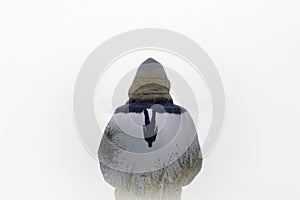 A double exposure of a moody, hooded figure with the reflection of a person standing by water