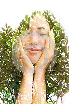 A double exposure portrait of a half smiling young woman with eyes closed holding her chin with hands and tree leaves