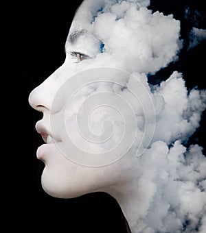 A double exposure portrait of a young woman's profile against black background with clouds