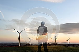 A double exposure of a silhouette of a man looking out on wind turbines at sunrise