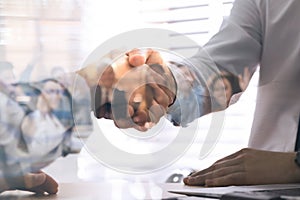 Double exposure of team workers and business partners shaking hands in office