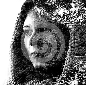 Double exposure of a young beautiful girl through the branches and leaves. Portrait of a woman, mysterious look, sad eyes, creativ