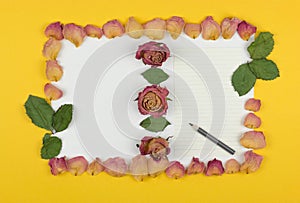 Double frame of dried rose petals on a white and yellow background with a sheet of paper and a pencil for your text