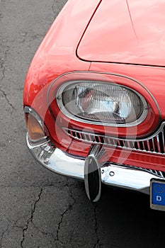 Double headlights with lots of chrome from a red American sports car classic from the 1950s