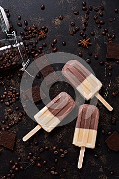 Double ice cream coffee vanilla. Ice cream on a stick with coffee beans and chocolate on a dark background. Top view