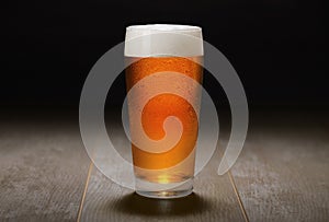 Double India pale ale beer served in a chilled pint glass on wooden counter at a craft beer pub, black background