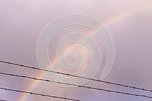 Double rainbow behind rows of a barbed wire