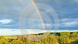 Double rainbow in cloudy blue sky after rain at sunset. A bright real rainbow against a hilly forest landscape in early spring.