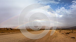 Double rainbow at the desert after the rain. Unsealed road suitable for 4wd cars. Dramatic sky with dark clouds. Mountains at the