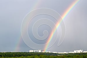 Double rainbow over green forest and urban houses