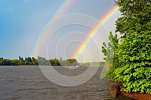 Double rainbow over the river after the rain, in the foreground green tree