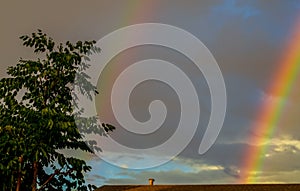 Double rainbow after the rain over the roof of rural house and trees