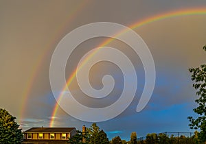 Double rainbow after the rain over the roof of rural house and trees