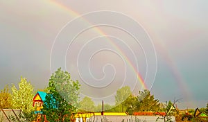 Double rainbow after rain over the roofs of rural houses and flowering trees on a spring or summer day. A beautiful natural