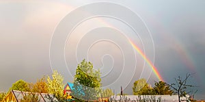 Double rainbow after rain over the roofs of rural houses and flowering trees on a spring or summer day. A beautiful natural