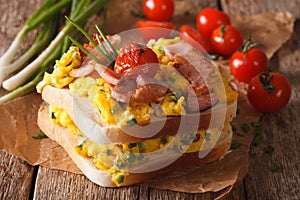 double sandwich with scrambled eggs, bacon and tomatoes close-up. Horizontal