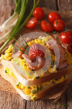 double sandwich with scrambled eggs, bacon and tomatoes close-up. vertical