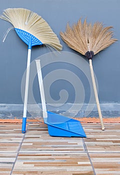 The double sweeping broom and the plastic dustpan are leaning against the sidewall of the house photo