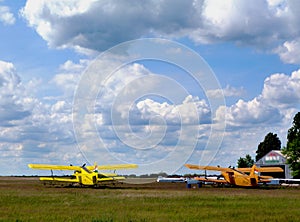 Double winged yellow airplanes in rural air field. blue sky and white clouds.