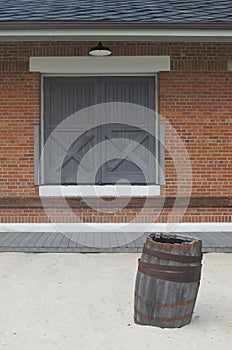 Double wood doors with X, red brick wall, and barrel on sand