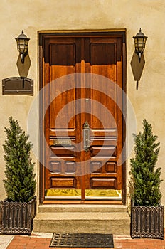 Double wooden doors and are flanked by twin light fixtures.