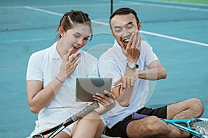 doubles tennis players laughing while sitting looking at tablet together