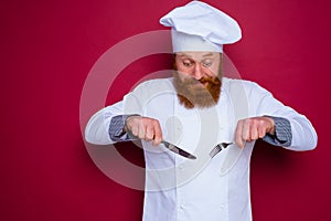 doubter chef with beard and red apron holds cutlery in hand