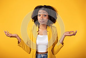 Doubtful black lady shrugging shoulders and spreading arms, unsure hesitant woman standing over yellow studio background