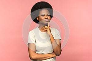 Doubtful black woman touching chin, frowning, pondering, looking at camera doubtfully, studio.