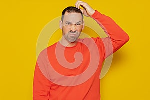 Doubtful Hispanic man thinking, scratching his head trying to find a solution, isolated on a yellow background.