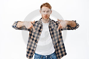 Doubtful man asking your opinion, what do you think. Redhead guy pointing fingers down, showing advertisement logo