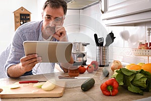 Doubtful man looking at recipe on a tablet at home