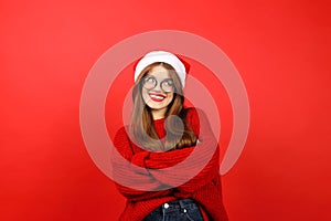 Doubting cheerful woman in santa hat on red background, confusedly thinking about Christmas gifts