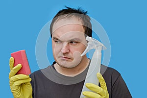 Doubting man cleaner in yellow gloves , portrait on studio blue background