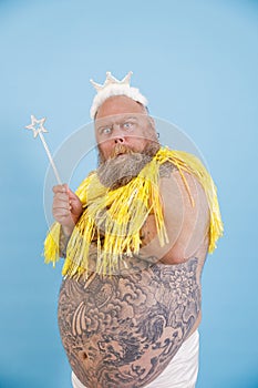 Doubting plus size man with crown and magic stick poses on light blue background