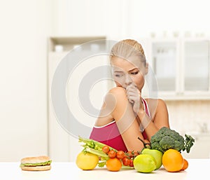 Doubting woman with fruits and hamburger