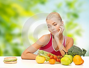 Doubting woman with fruits looking at hamburger